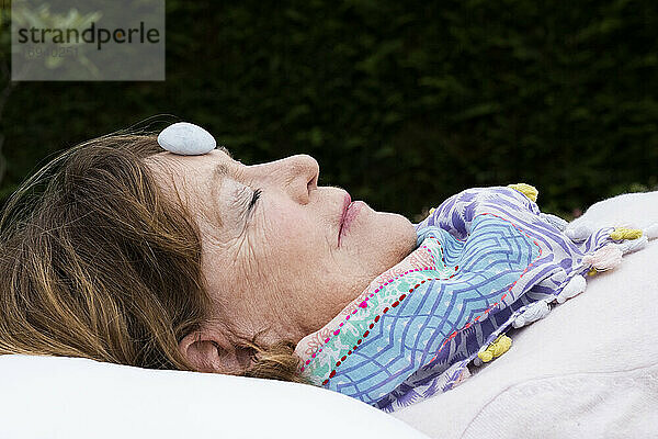 Frau mit Stein auf der Stirn während einer alternativen Therapiesitzung in einem Garten.