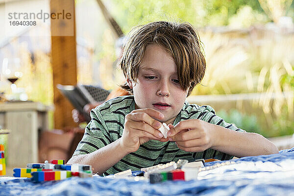 7 Jahre alter Junge spielt mit Bauklötzen auf einer Terrasse