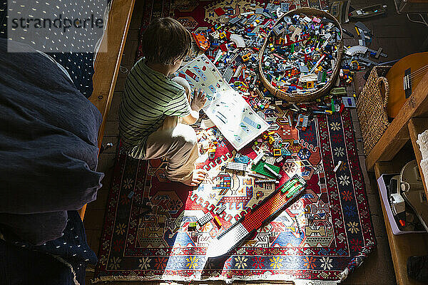 Junge sitzt zwischen Spielzeug auf seinem Schlafzimmerboden in einem Fleck Sonnenlicht