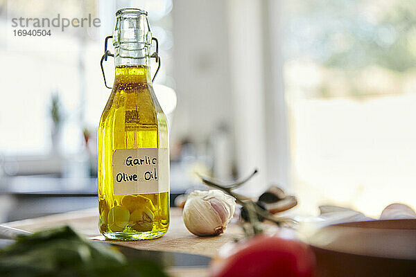Glasflasche mit Olivenöl und Knoblauchzehen auf dem Schneidebrett in der Küche stehend