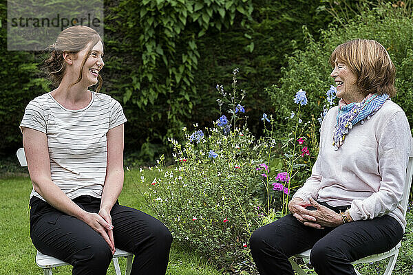 Frau und weibliche Therapeutin bei einer alternativen Therapiesitzung in einem Garten sitzend.