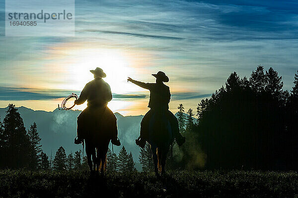 Zwei Cowboys reiten über Grasland mit Bergen im Hintergrund  früher Morgen  Britisch-Kolumbien  Kanada.