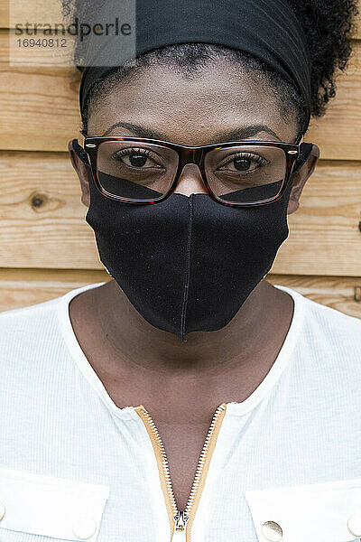 Porträt einer schwarzen Frau mit Brille und Gesichtsmaske  die in die Kamera schaut.