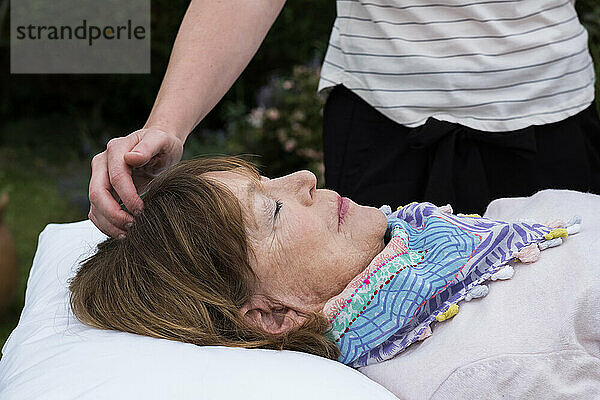 Reiki-Therapeut mit einem Klienten in einer Therapiesitzung  der Meridianpunkte am Körper berührt.