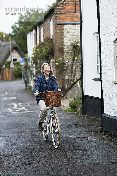 Junge blonde Frau auf dem Fahrrad in einer Dorfstraße.