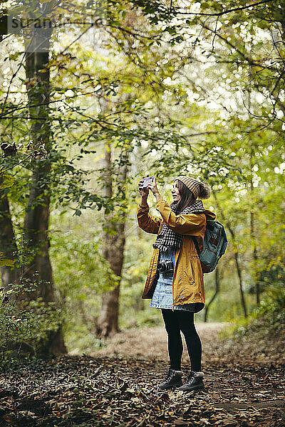 Frau steht auf einem Waldweg und fotografiert mit einem Smartphone
