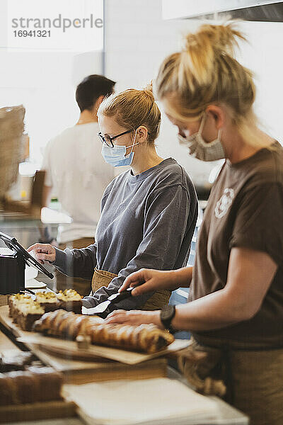 Kellnerin mit Gesichtsmaske  die in einem Café arbeitet und Essen zubereitet.