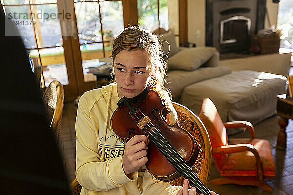 Teenager-Mädchen zupft Saiten ihrer Geige zu Hause