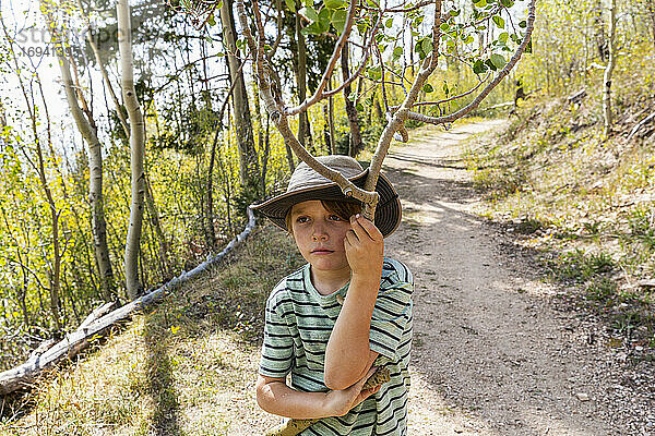 7 Jahre alter Junge hält gebrochenen Ast im Wald von Aspen-Bäumen