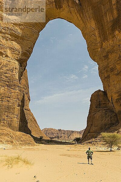 Mann steht unter drittgrößtem Felsbogen der Welt  Ennedi-Plateau  Tschad  Afrika