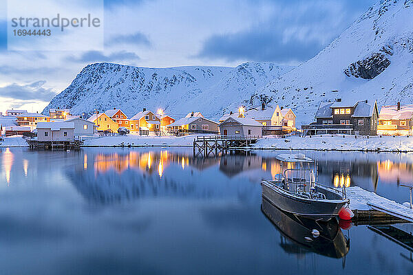 Beleuchtetes Dorf Sorvaer spiegelt sich in der kalten See während der Winterdämmerung  Insel Soroya  Troms og Finnmark  Nordnorwegen  Skandinavien  Europa