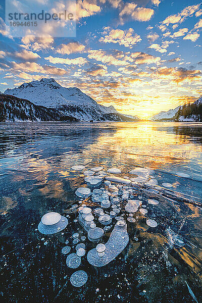 Wolken am brennenden Himmel bei Sonnenuntergang auf dem Piz Da La Margna und Eisblasen  die im Silser See gefangen sind  Engadin  Graubünden  Schweiz  Europa