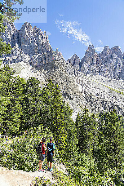 Rückansicht von zwei jungen Wanderern  die die Geisler vom berühmten Adolf-Munkel-Weg aus bewundern  Val di Funes  Südtirol  Dolomiten  Italien  Europa