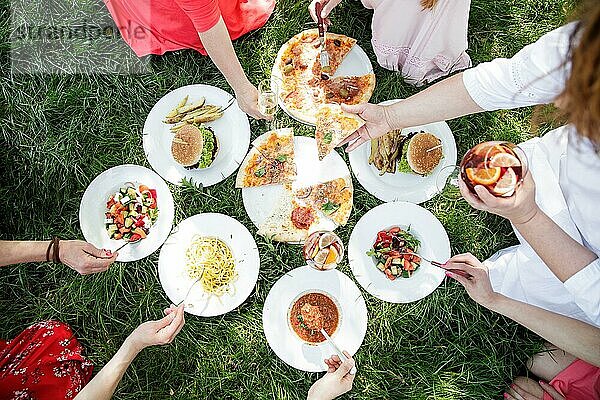 Gruppe von Frauen genießen verschiedene Speisen im Gras  Pizza  Burger  Salate  Pasta  Suppe