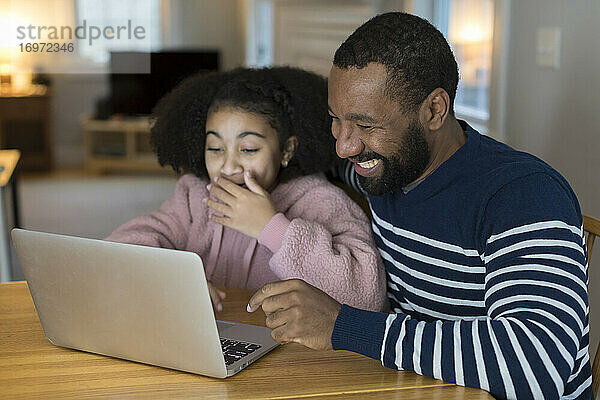 Afroamerikanischer Vater und seine Tochter lachen über den Laptop