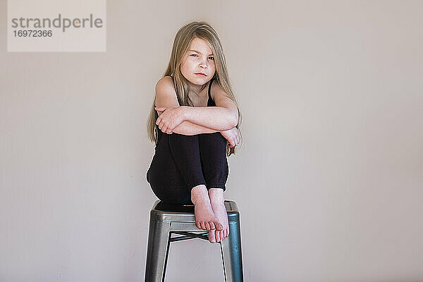 Junges Mädchen sitzt auf einem Hocker im Haus