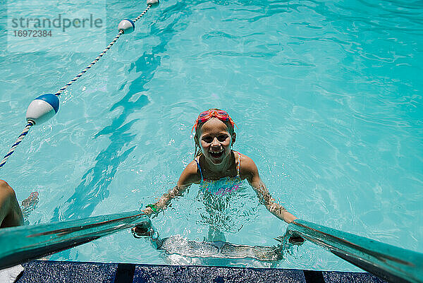 Kleines Mädchen schaut von der Pool-Leiter im Wasser auf