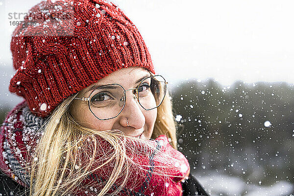 Lächelnde Frau trägt Wollmütze und Schal in einem kalten Wintertag. Glückliches Mädchen in einem Pullover im Freien im Schnee.