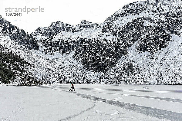 Ganzkörper-Hockeyspieler mit Schläger auf gefrorenem See in der Nähe eines verschneiten Bergrückens im Winter in British Columbia  Kanada