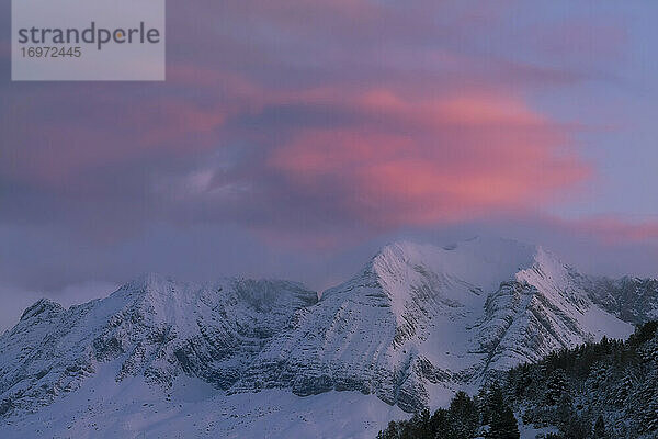 Farbwolken zwischen Bergen in einer verschneiten Landschaft bei Sonnenuntergang