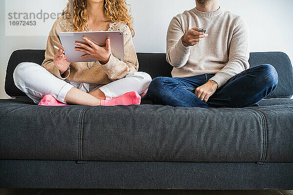 Crop-Paar auf dem Sofa mit Tablet und TV-Fernbedienung