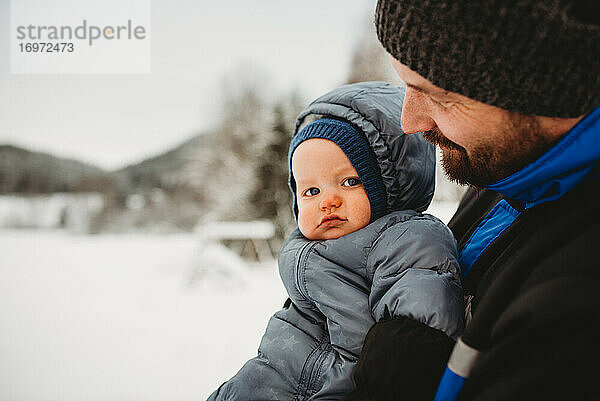 Nahaufnahme von Papa mit Baby im Schneeanzug im Winter mit Schnee