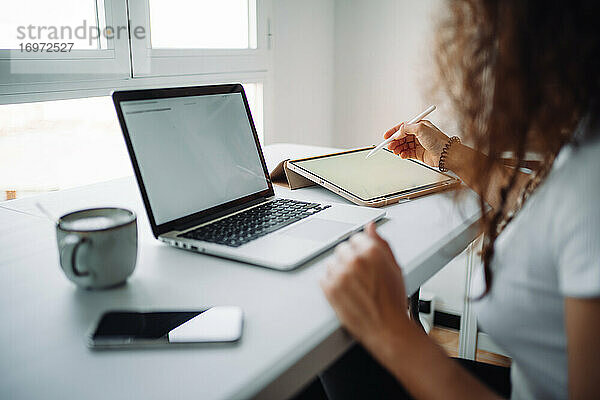 Junge Frau arbeitet von zu Hause aus mit einem Laptop  einem Smartphone und einem Tablet  während sie einen Kaffee trinkt