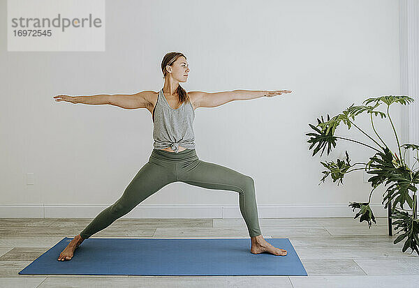 Athletische Frau macht Krieger-Yoga-Pose drinnen auf blauer Matte