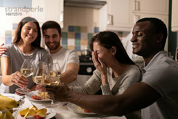 Junge Frau lacht beim Weintrinken mit Freunden und schwarzem Freund