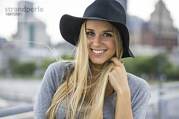 Blonde Frau lächelnd mit Hut und Stadtsilhouette hinter ihr