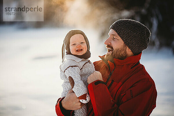 Vater hält schönes lächelndes Baby draußen im Schnee in Skandinavien