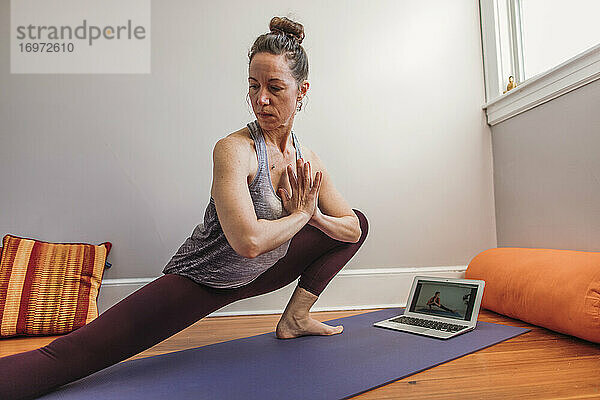 Sportliche Frau nutzt zu Hause Computer für Online-Yoga-Unterricht