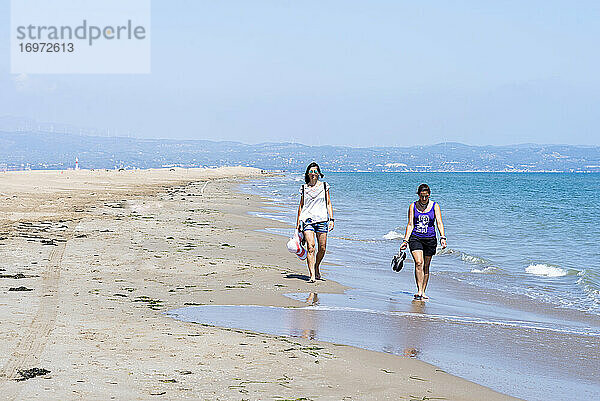 Vorderansicht von zwei Frauen  die barfuß am Strand laufen