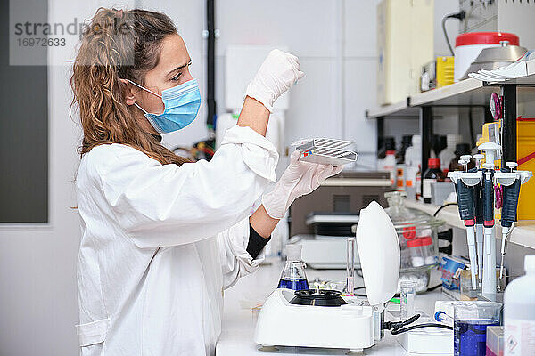 Junge Wissenschaftlerin  die in einem Labor arbeitet und mit einer Zentrifuge DNA-Proben in einem Reagenzglas nimmt. Konzept der Laborforschung.
