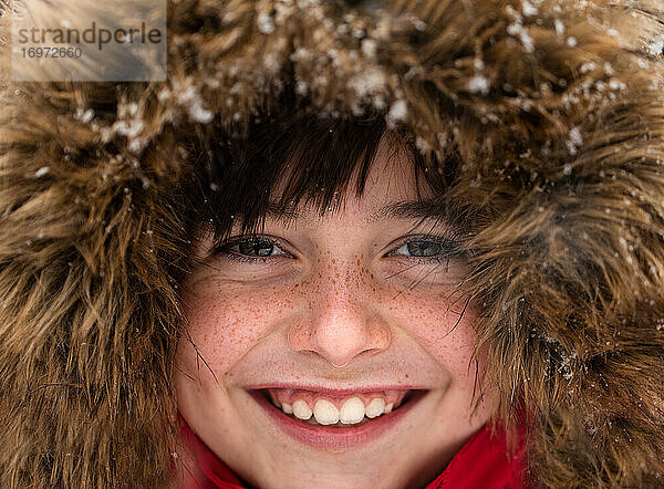 Nahaufnahme eines niedlichen  lächelnden Jungen mit Fellkapuze an einem verschneiten Tag.