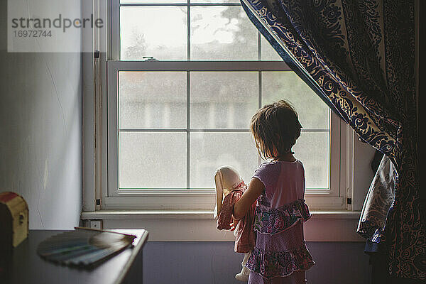 Ein kleines Kind steht am Schlafzimmerfenster und hält zärtlich einen ausgestopften Hasen