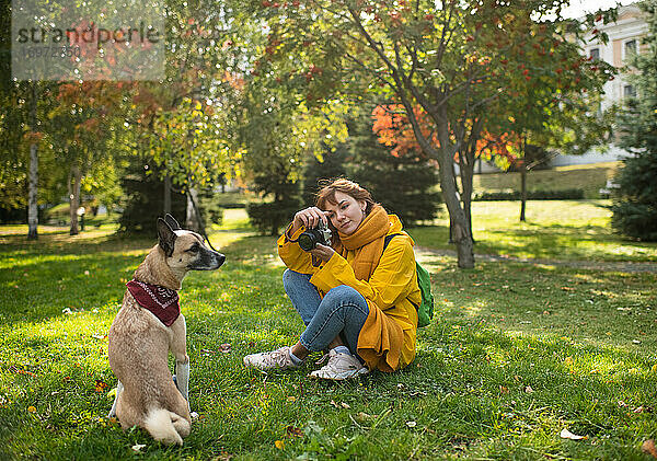 Freudige Frau  die ihren Hund im Park fotografiert