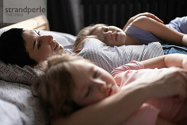 Mutter umarmt schlafende Töchter am Morgen zu Hause
