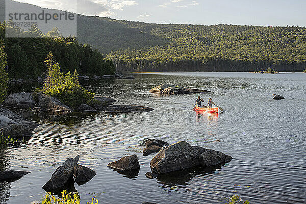 Ehepaar paddelt mit rotem Kanu zwischen Felsen auf einem See in der Wildnis von Maine