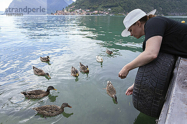 Eine Frau lehnt sich über einen Steg und füttert einige Enten auf einem See in Italien