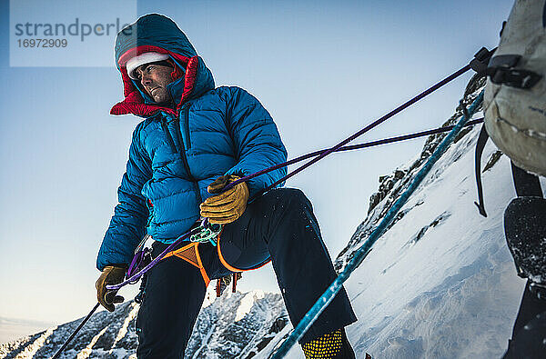 Männlicher Kletterer sichert seinen Vorsteiger bei einer kalten alpinen Wintertour