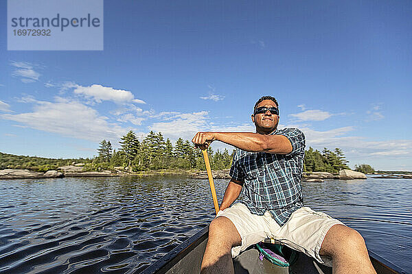 Afrikanischer Mann paddelt Kanu entlang des felsigen Ufers eines Teiches in Maine