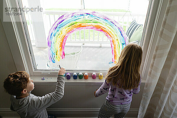 Ansicht von oben auf Geschwister  die einen Regenbogen auf das Wohnzimmerfenster malen