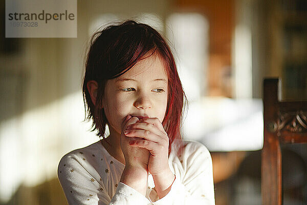 Ein schüchternes kleines Mädchen mit rot gefärbten Haaren sitzt allein mit gefalteten Händen da