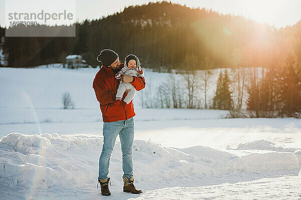 Papa und süßes Baby im Wald voller Schnee im Winter bei Sonnenuntergang