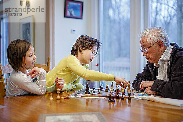 Ein Junge und seine Schwester sitzen am Schachbrett und der Großvater macht einen Zug