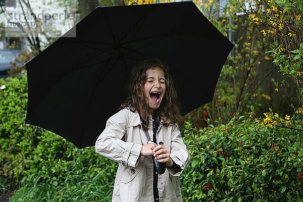 Ein Mädchen mit langen lockigen Haaren unter einem Regenschirm lächelt breit.