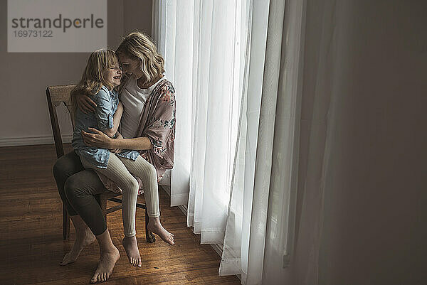 Mutter und Tochter sitzen eng beieinander am Fenster im Atelier