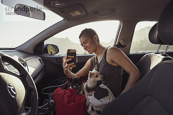 Glückliche Person mit zwei Hunden auf dem Schoß im Auto macht Fotos mit Telefon Spanien