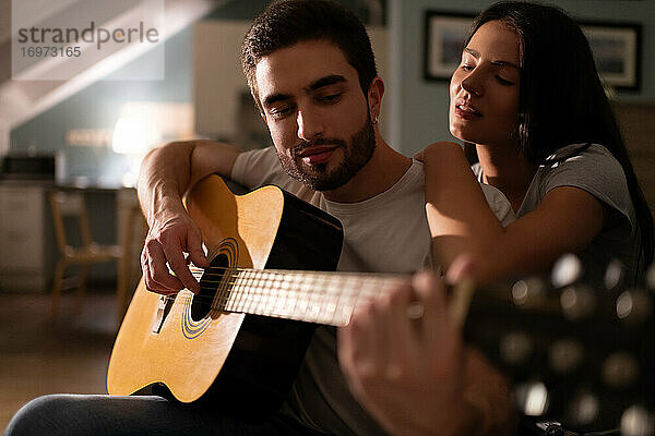Junge Frau hört ihrem Freund beim Gitarrenspiel zu